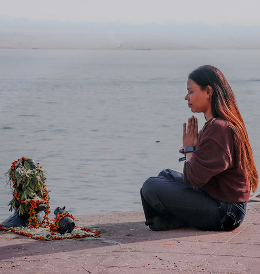 Woman praying by a decorated stone structure near water